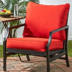 a red chair sitting on top of a brick patio next to a table with fruit