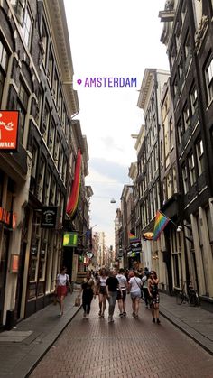 several people walking down an alley way with buildings in the background and a sign that reads amsterdam