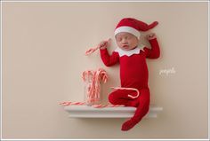 a baby wearing a santa hat laying on top of a shelf next to candy canes