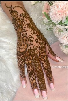 a woman's hand with henna on it and some flowers in the background