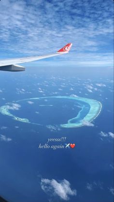 an airplane wing flying over the ocean with a heart shaped island in the middle of it