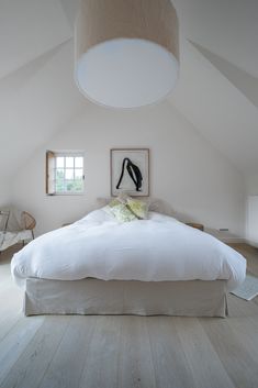 a large white bed sitting in a bedroom next to a painting on the wall above it