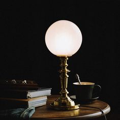 a lamp sitting on top of a wooden table next to a book and coffee cup