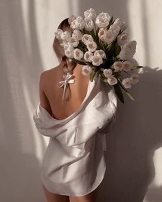 a woman in a white dress holding a bunch of flowers on her head and back