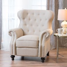 a white chair sitting in front of a window next to a table with a lamp on it