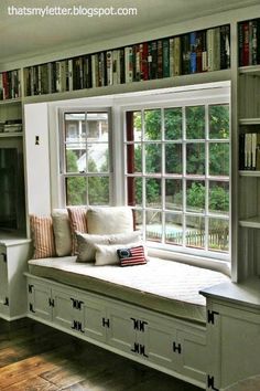 a window seat in the corner of a room with bookshelves and cabinets on either side