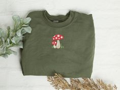 This comfy and cute shirt will soon become your new favorite to wear. A cute little mushroom design is embroidered on the front center.  This is a unisex fit crew neck sweatshirt.  Please refer to the size chart for measurements to ensure a correct fit.  This comfy and cozy crew neck sweatshirt features: - 8 oz.(US) 13.3 oz.(CA), 50/50 preshrunk cotton/polyester - Heather Sport colors: 60/40 polyester/cotton - Air jet yarn = softer feel and reduced pilling - Double needle stitching at shoulder, armhole, neck, waistband and cuffs - 1 x 1 rib with spandex Cotton Fall Sweatshirt With Mushroom Print, Cotton Sweatshirt With Mushroom Print, Cotton Crew Neck Sweatshirt With Mushroom Print, Cotton Sweatshirt With Mushroom Print For Fall, Casual Crew Neck Sweatshirt With Mushroom Print, Winter Cotton Tops With Mushroom Print, Cottagecore Cotton Crew Neck Sweatshirt, Cotton Long Sleeve Sweatshirt With Mushroom Print, Casual Long Sleeve Top With Mushroom Design