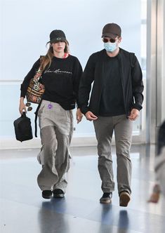 a man and woman walking through an airport wearing face masks to protect them from the sun