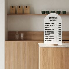 a coffee menu board sitting on top of a wooden counter next to cups and mugs