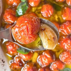 a spoon full of tomatoes and other vegetables with sauce in it, on top of a table