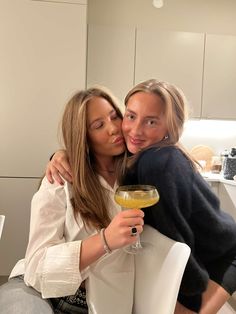 two women hugging each other while holding a wine glass in front of their face and looking at the camera