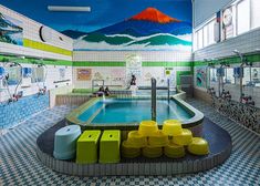 an indoor swimming pool with colorful tiles on the walls and floor, surrounded by yellow stools