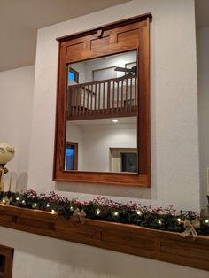 a mirror is hanging on the wall above a mantel with christmas garland and lights