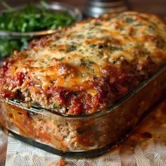 a casserole dish with meat and cheese in it on a table next to vegetables