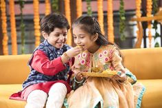 two children sitting on a yellow couch eating food from a plate in front of them