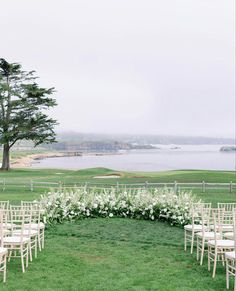 an outdoor ceremony setup with chairs and flowers in the foreground, overlooking a body of water