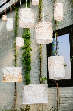 paper lanterns are hanging from the ceiling in front of a brick wall with ivy growing on it