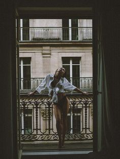 a woman standing on a balcony in front of a window with her arms stretched out