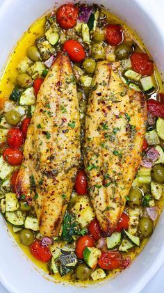 two fish fillets in a white bowl with tomatoes, cucumbers and olives