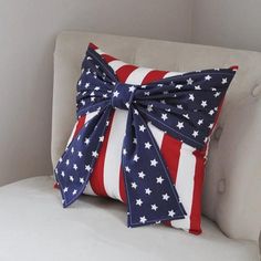 an american flag pillow with a bow on it sitting on a white chair in front of a gray wall