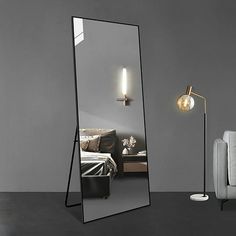 a mirror sitting on top of a floor next to a chair and lamp in a room