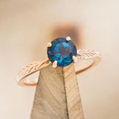 a ring with a blue stone on top of it sitting on a piece of wood