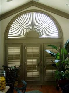 an arched window with shutters in the middle and potted plants on the other side