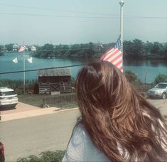 a woman with long hair standing in front of a lake and an american flag on top of her head