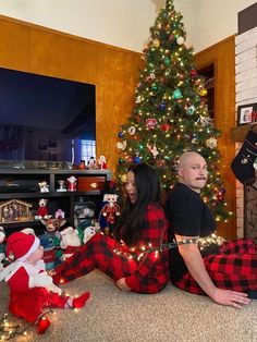 a man and woman sitting in front of a christmas tree