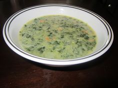 a white bowl filled with broccoli soup on top of a wooden table