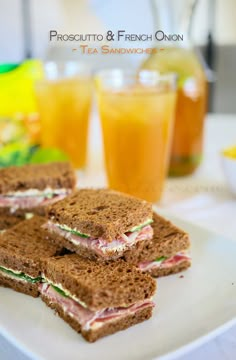 three sandwiches on a white plate with orange juice in the background and two glasses of lemonade