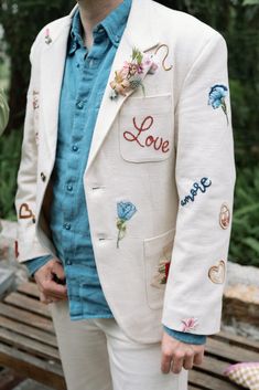 a man in a white suit with embroidered words on the front and chest, standing next to a wooden bench