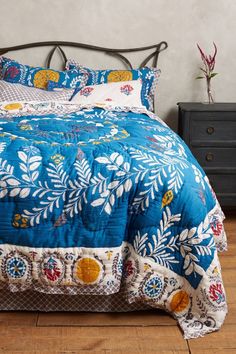 a bed with blue and white bedspread on top of wooden floor next to dresser