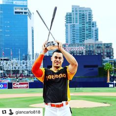 a baseball player holding up a trophy on top of a field in front of a cityscape