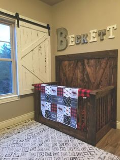 a baby crib in the corner of a room with a bed and wooden name sign on the wall