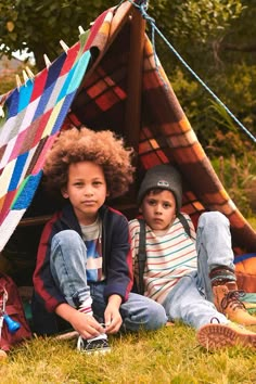 two young children sitting in front of a teepee