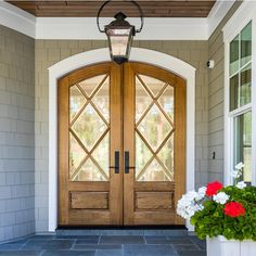 the front door to a house with two large wooden doors and flowers on the side