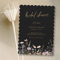 a black and gold bridal shower card with flowers on the front, along with a white flower in the middle