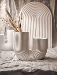 three white vases sitting on top of a bed with dried plants in the middle