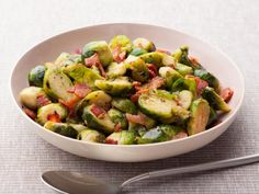 a white bowl filled with brussel sprouts and bacon next to a spoon