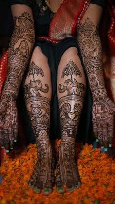 the legs and feet of a woman with henna tattoos on their hands, sitting in front of flowers