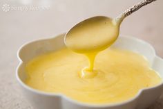 a spoon full of yellow liquid being poured into a white bowl