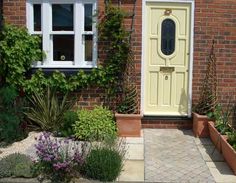 a yellow door in front of a brick building with plants and flowers around the entrance