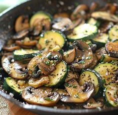 a skillet filled with mushrooms and zucchini on top of a wooden table