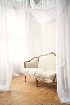 a white couch sitting on top of a hard wood floor next to a curtained window