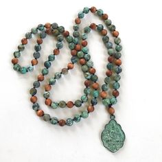 "A Mala for positive change, this Buddha pendant Mala bead necklace from True Nature Jewelry is hand knotted to perfection. It features matte African Turquoise beads that are said to open the mind to new ideas and possibility and help develop positive change in our lives. Sandalwood can be added as a accent bead. A good Mala for working with the Third Eye Chakra, helping to stimulate, and strengthen and clear the center while allowing growth. The unique Buddha pendant dangles with effortless gra Turquoise Jewelry With 8mm Beads For Festival, Turquoise Beaded Jewelry For Festival, Adjustable Spiritual Turquoise Necklace For Meditation, Turquoise Spiritual Beads For Meditation, Spiritual Beaded Turquoise Necklace For Jewelry Making, Spiritual Turquoise Beads For Meditation, Turquoise Spiritual Beads With Natural Stones, Spiritual Turquoise Beads With Natural Stones, Turquoise Spiritual Polished Beads