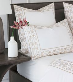 a vase with flowers on a bed next to two pillows and a pillow case in the corner