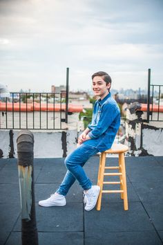 a man sitting on top of a wooden stool next to a metal pole and fence