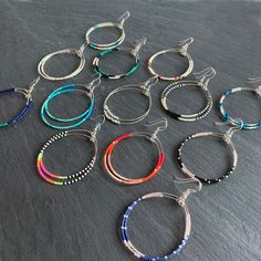 six pairs of hoop earrings with multicolored beads and silver findings on a slate surface