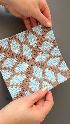 two hands are holding a piece of crocheted material that is blue and brown